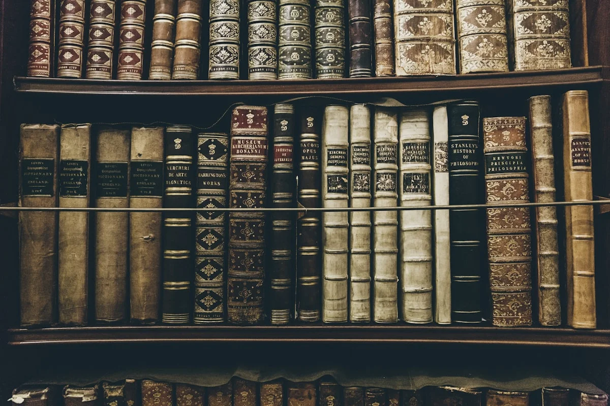 Antique leather-bound volumes with ornate gold lettering on dark wooden shelves